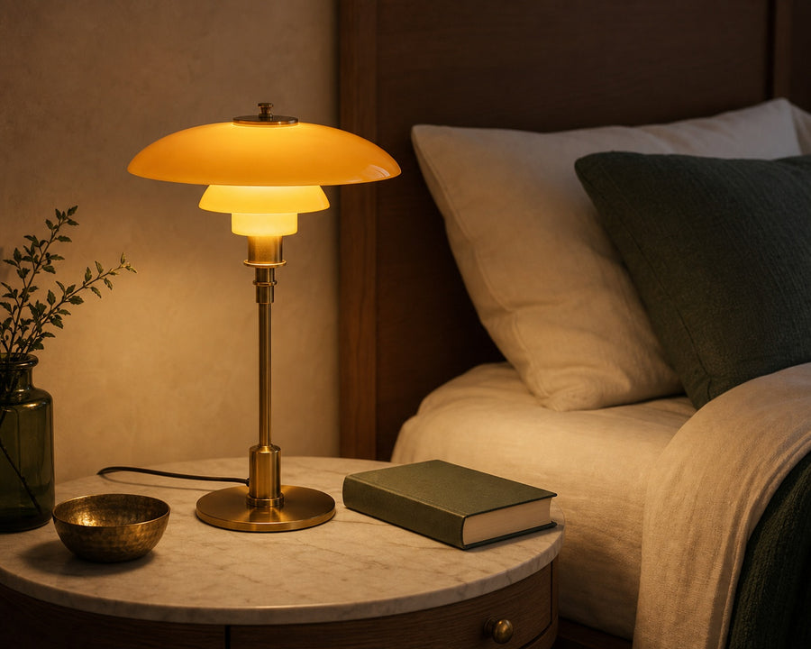The glass table lamp glowing on a bedside table