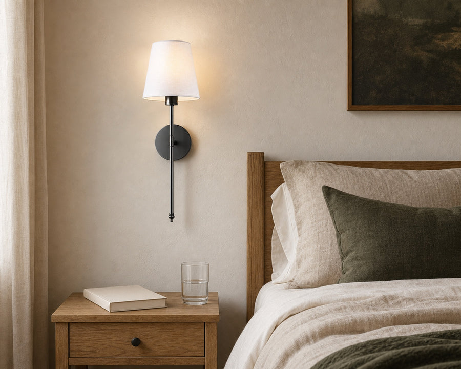 A bedside table left clear with the sconce on the wall above